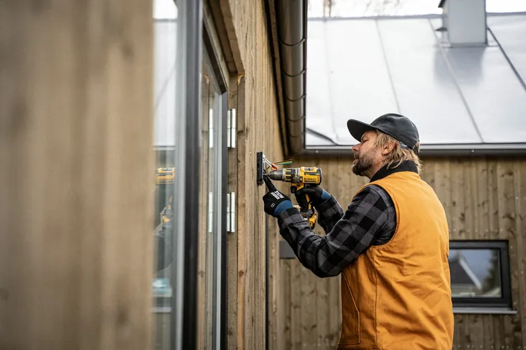 Electrician mounting an electrical box on a home exterior